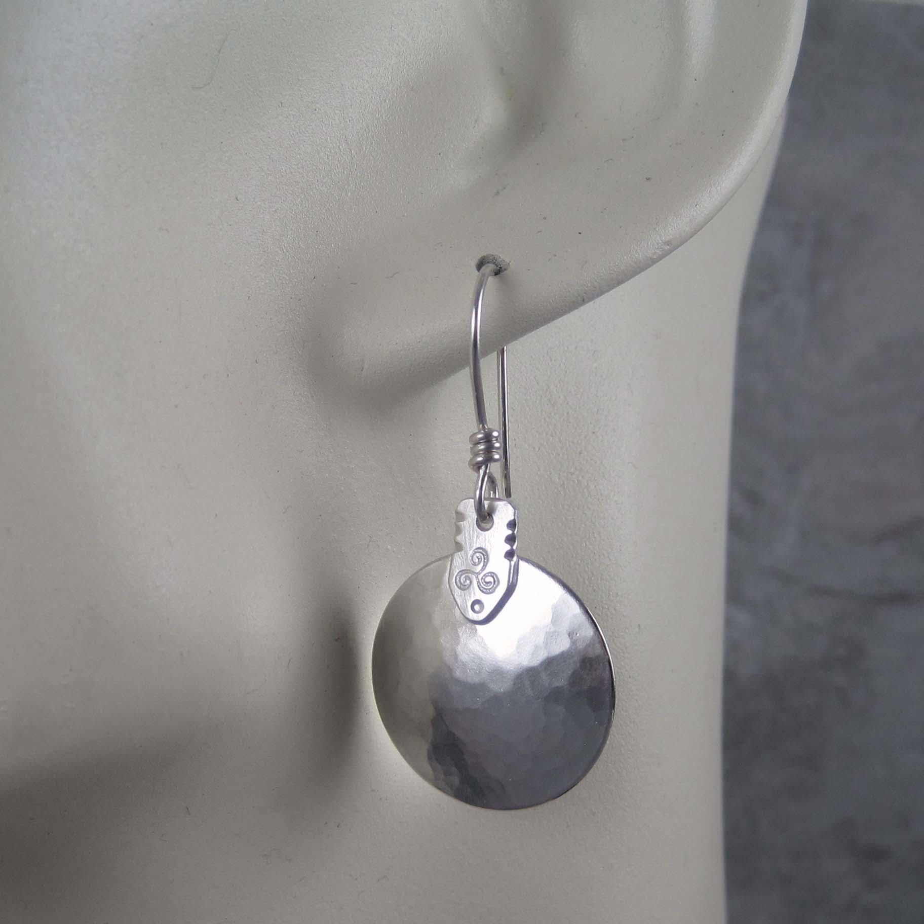 Silver earrings on a mannequin ear with a neutral background