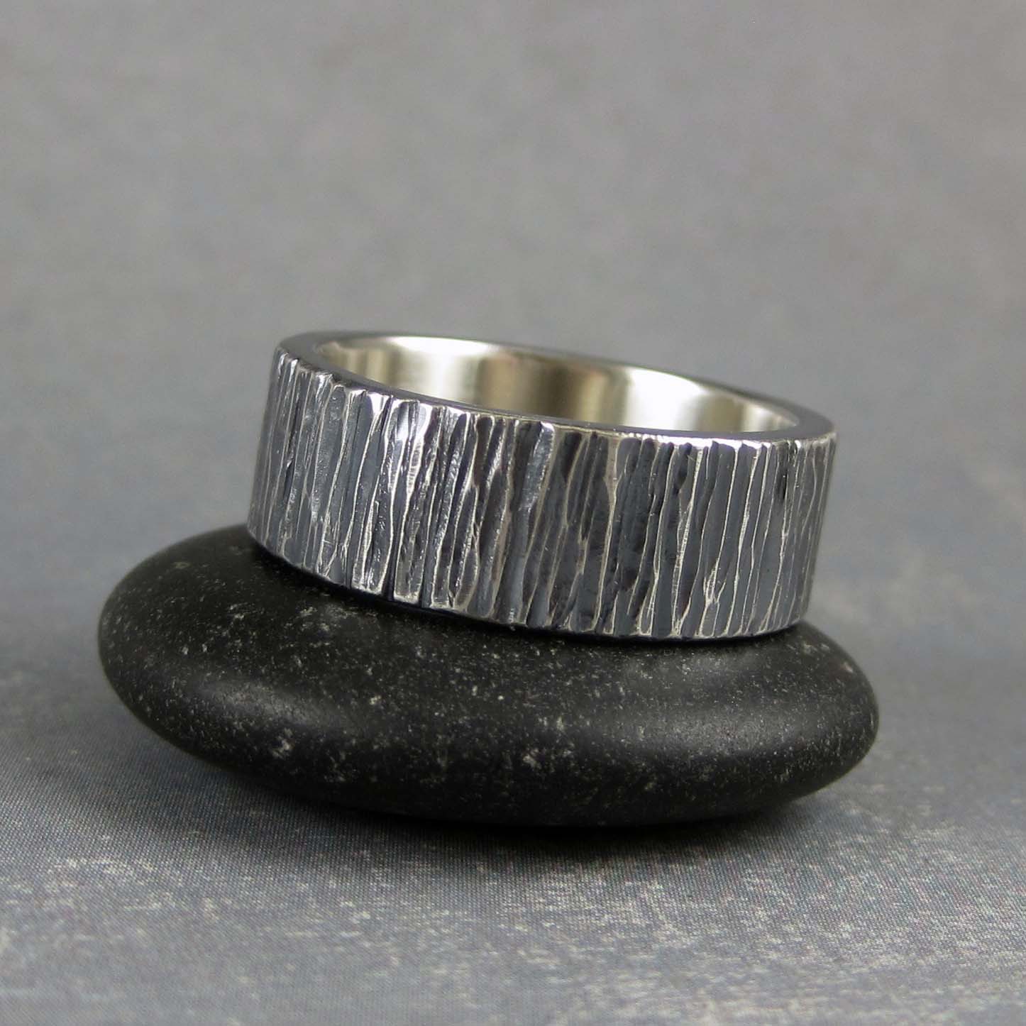 Handmade silver ring with textured band on a black stone against a gray background