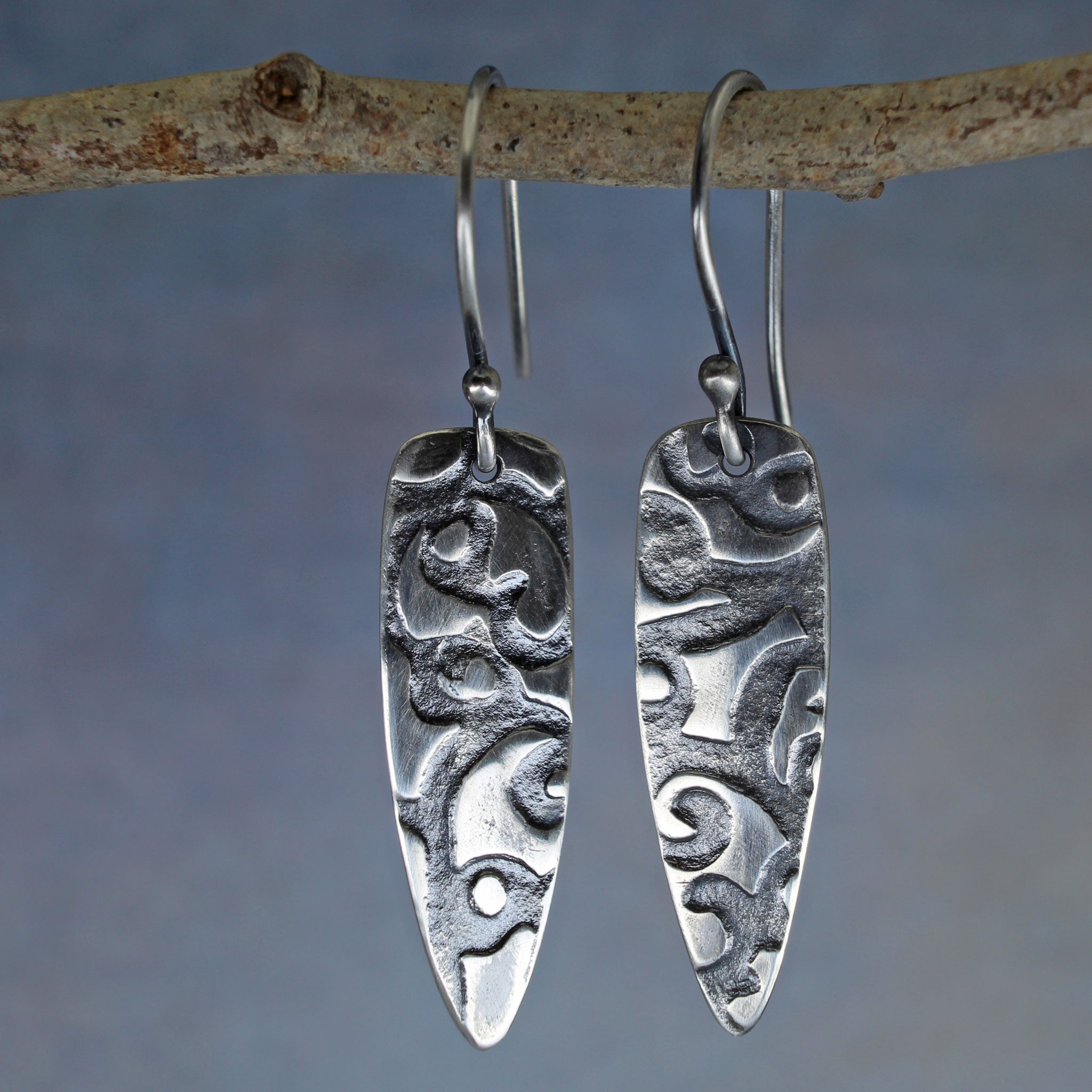 Sterling silver shield earrings with deep abstract texture and dark patina.
