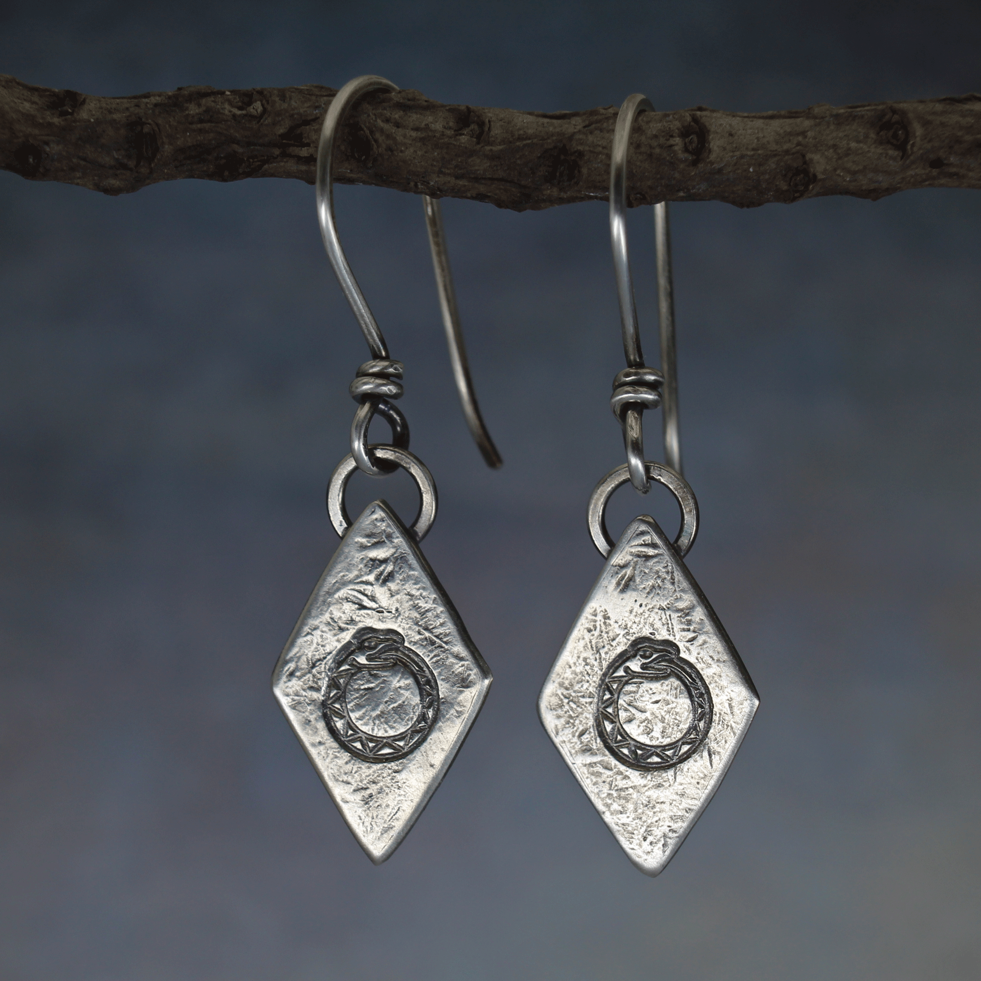 Ouroboros earrings with light patina highlighting stamped serpent-circle detail