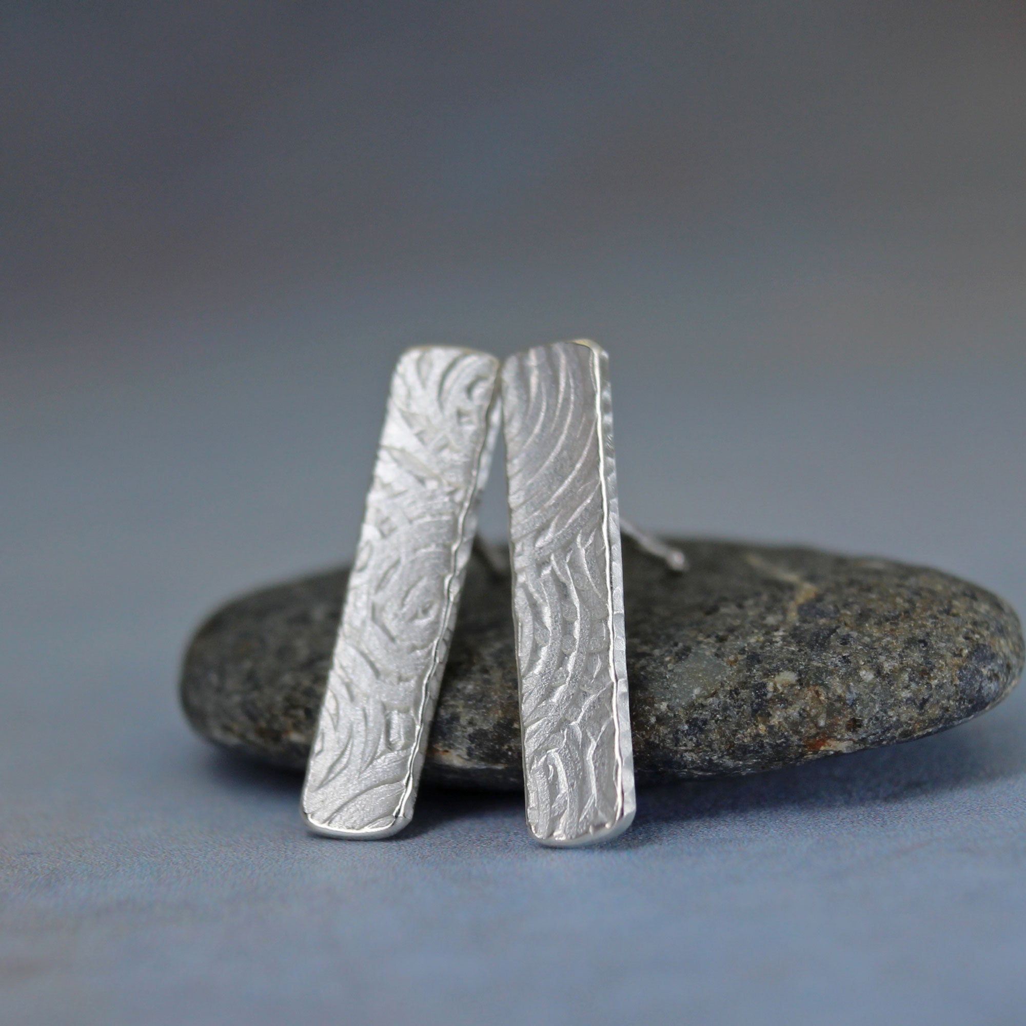 Silver earrings with textured spiral design on a stone surface