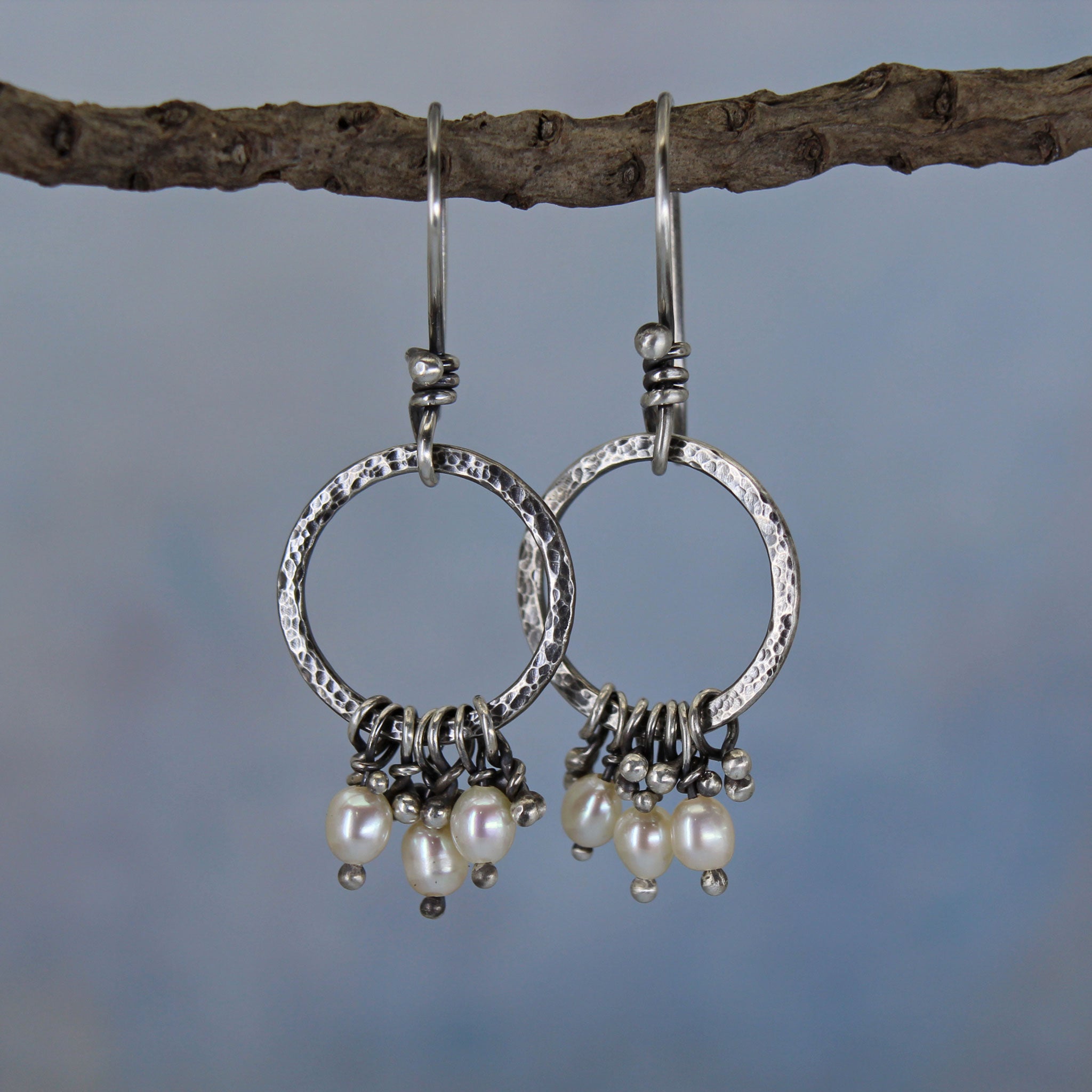 Handmade sterling silver circle earrings with white freshwater pearls, shown hanging from a branch