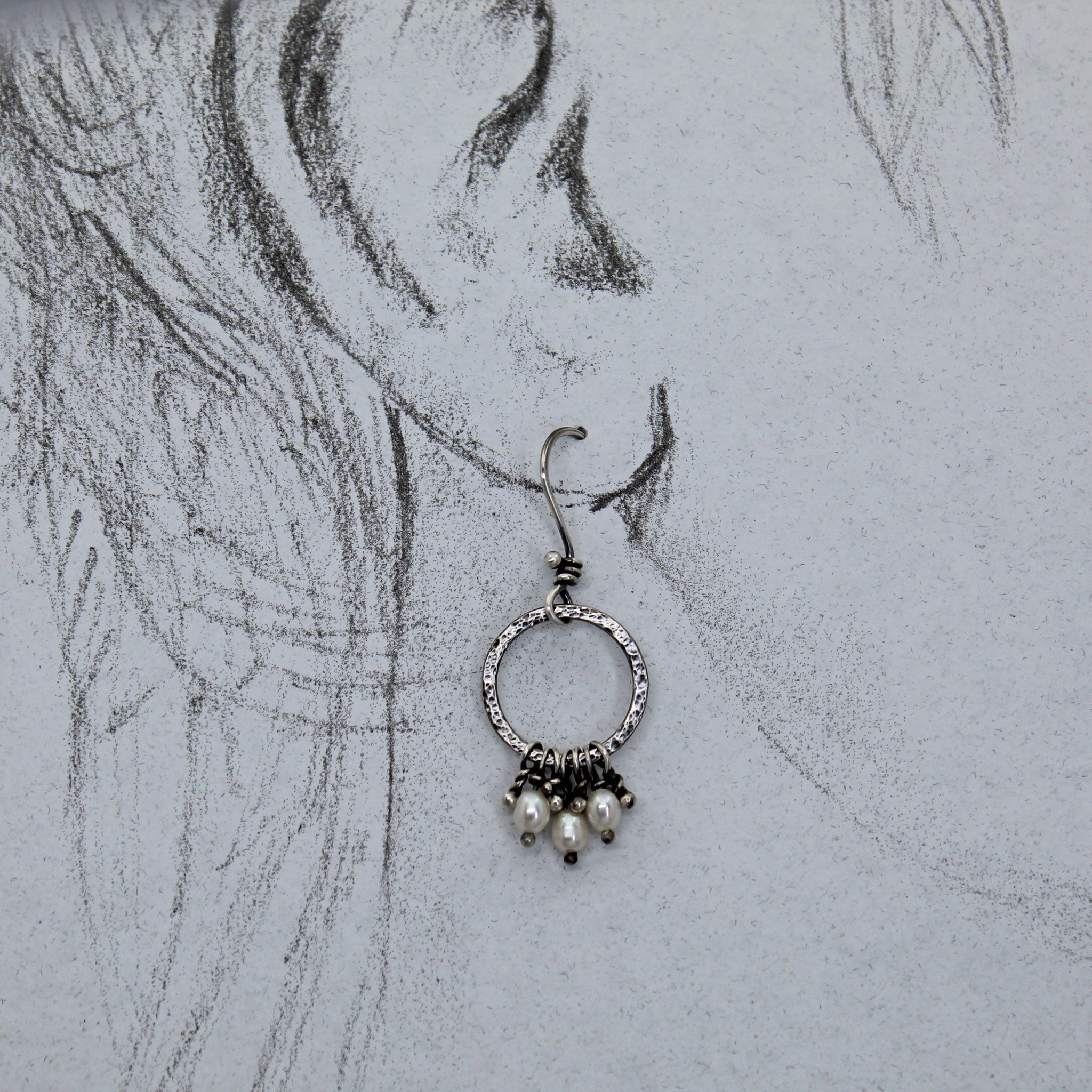 Silver earring with pearls on a pencil sketch of a life size ear