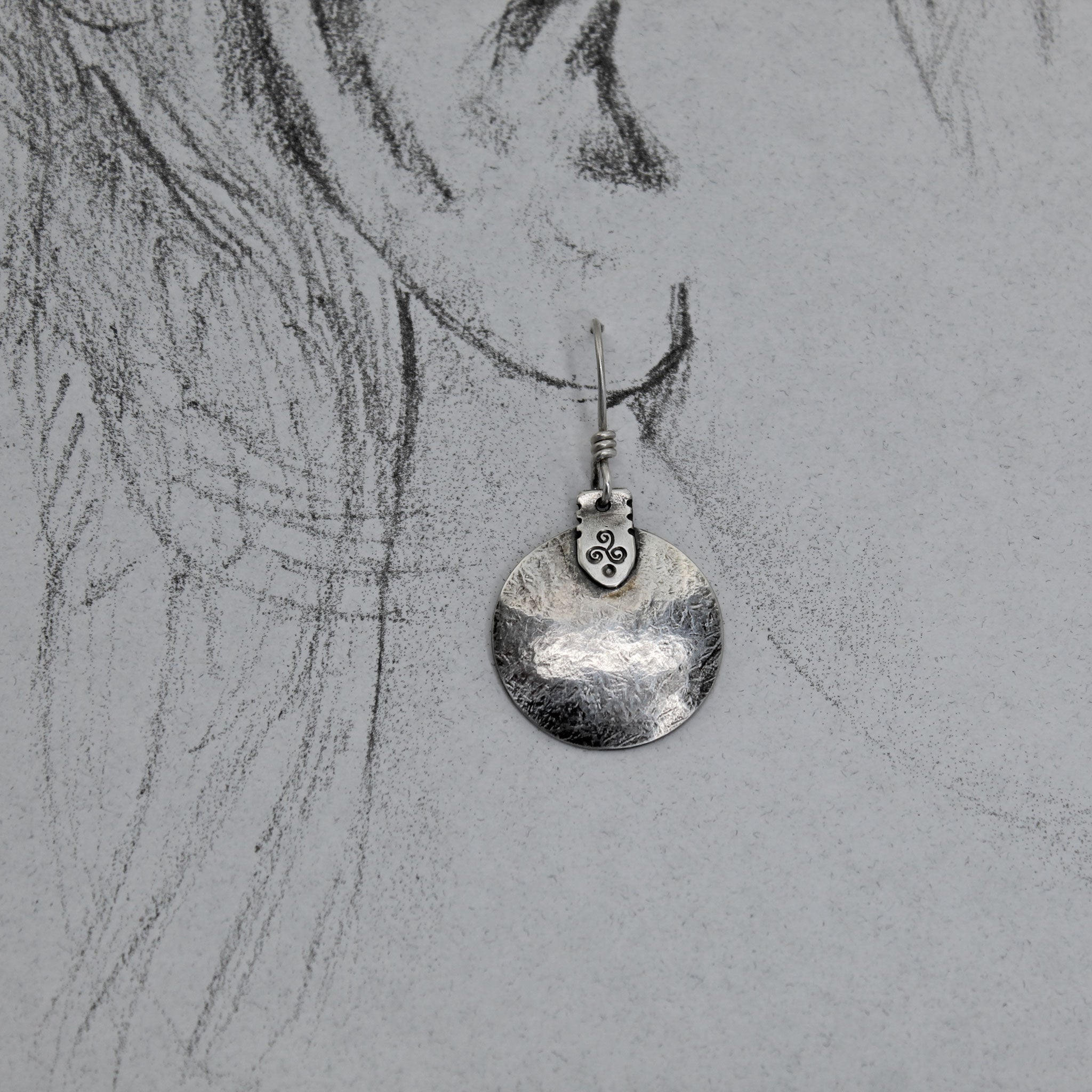 Triskele disc earrings shown on life size drawing of an ear.