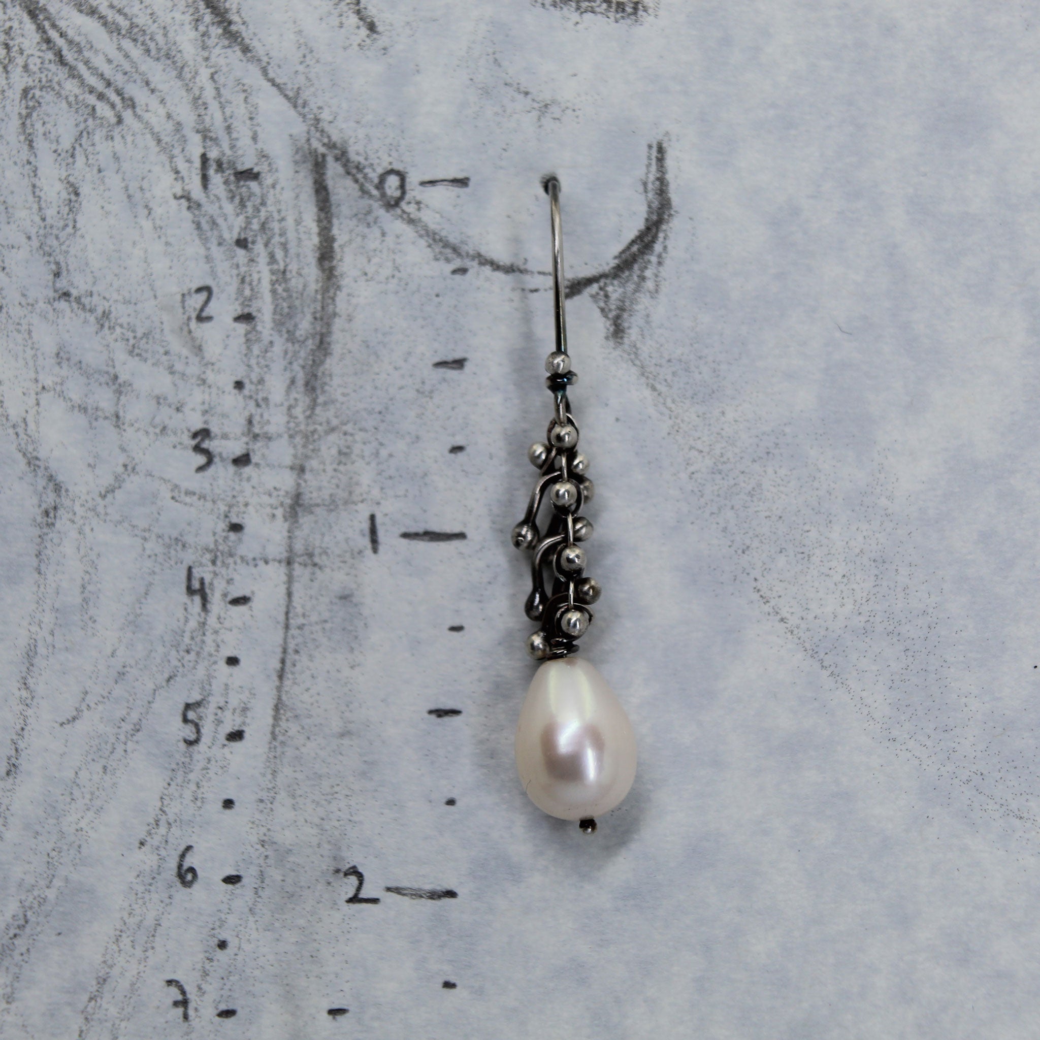 Pearl earring on a life size drawing of an ear with measurement scale