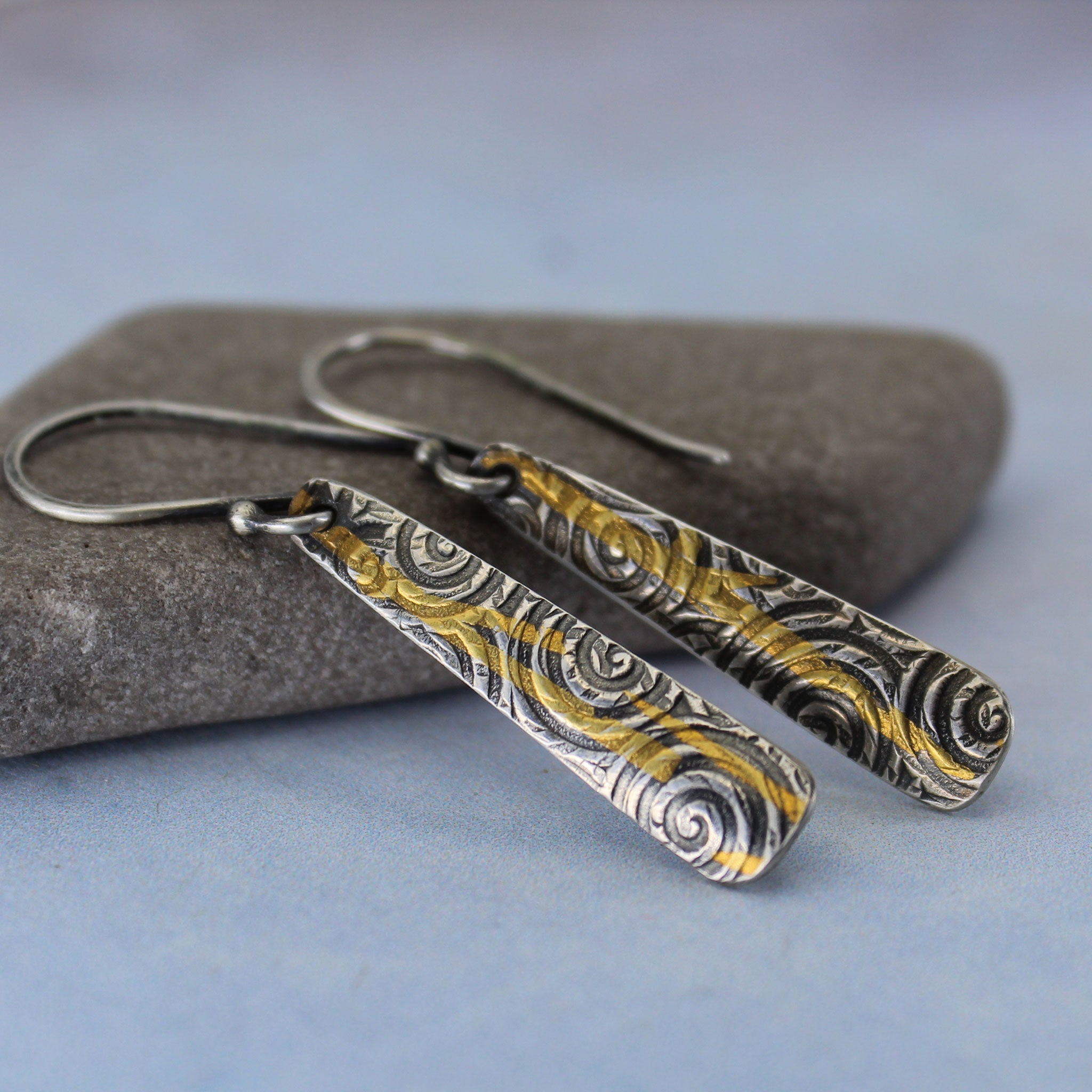 Pair of silver and gold patterned earrings on a stone surface