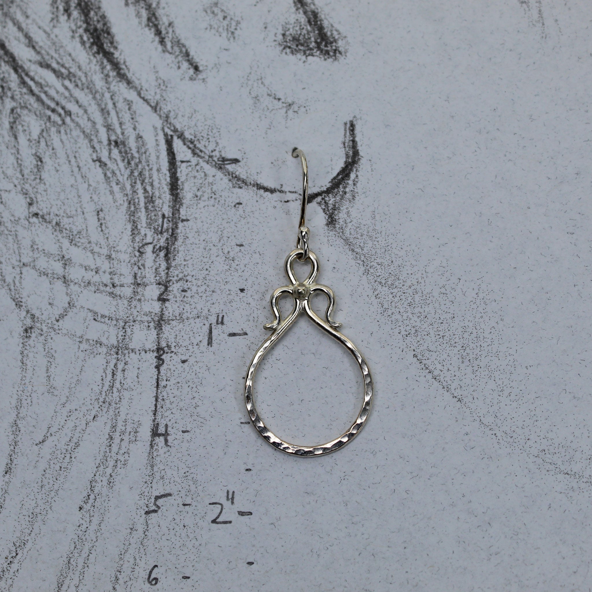 Unique sterling silver earrings shown on pencil drawing of a life size ear