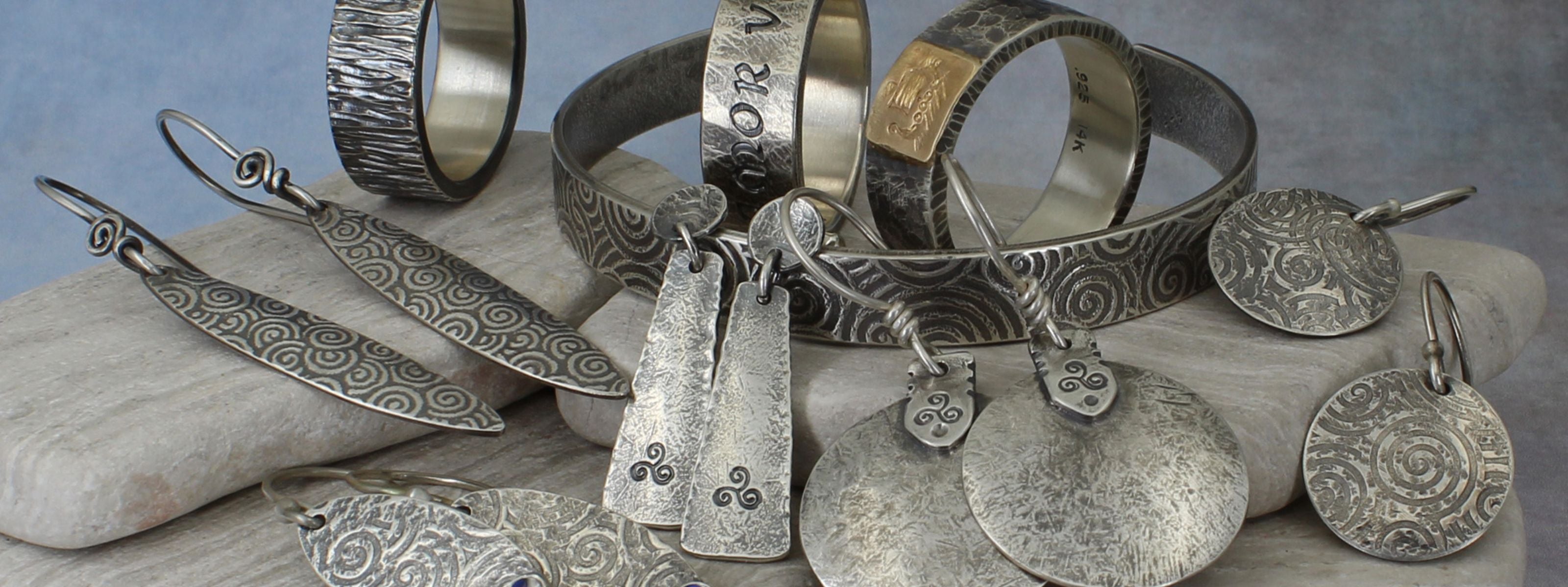 Collection of handmade ancient style silver jewelry including earrings and bracelets on a stone surface.