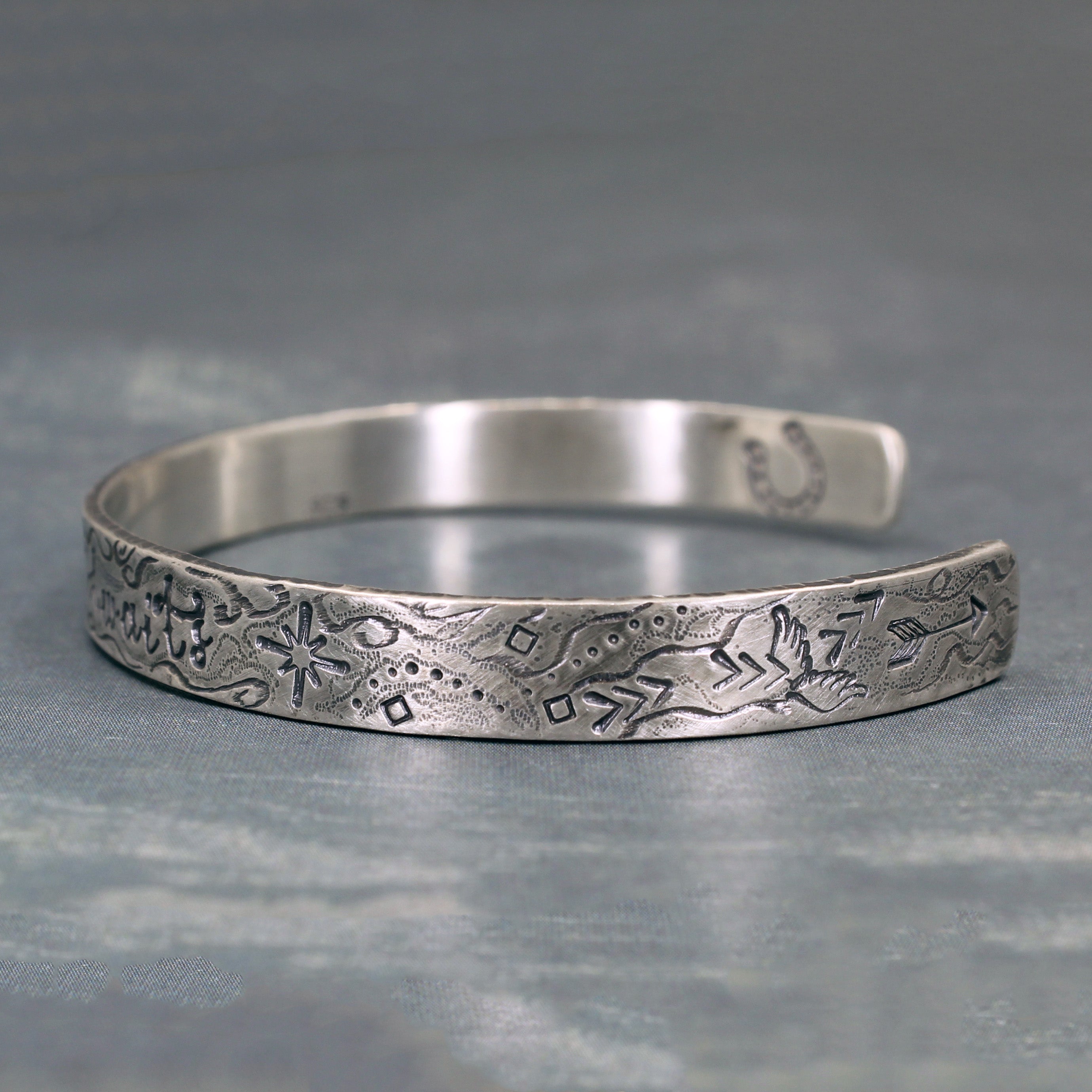 Close-up of symbolic stamps on silver cuff – star, arrow, wings, and horseshoe detail