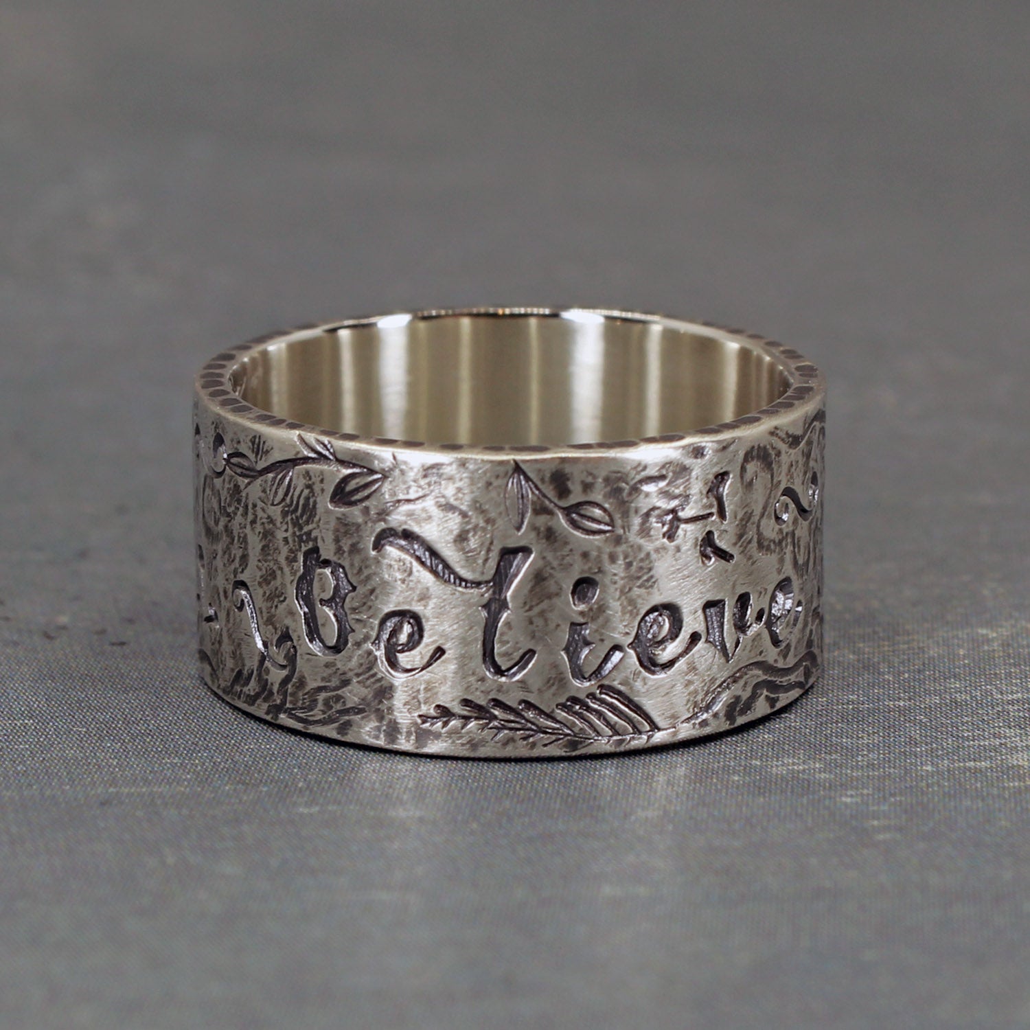 Sterling silver ring stamped with the word “Believe” and uplifting symbols including stars, hearts, and flowers