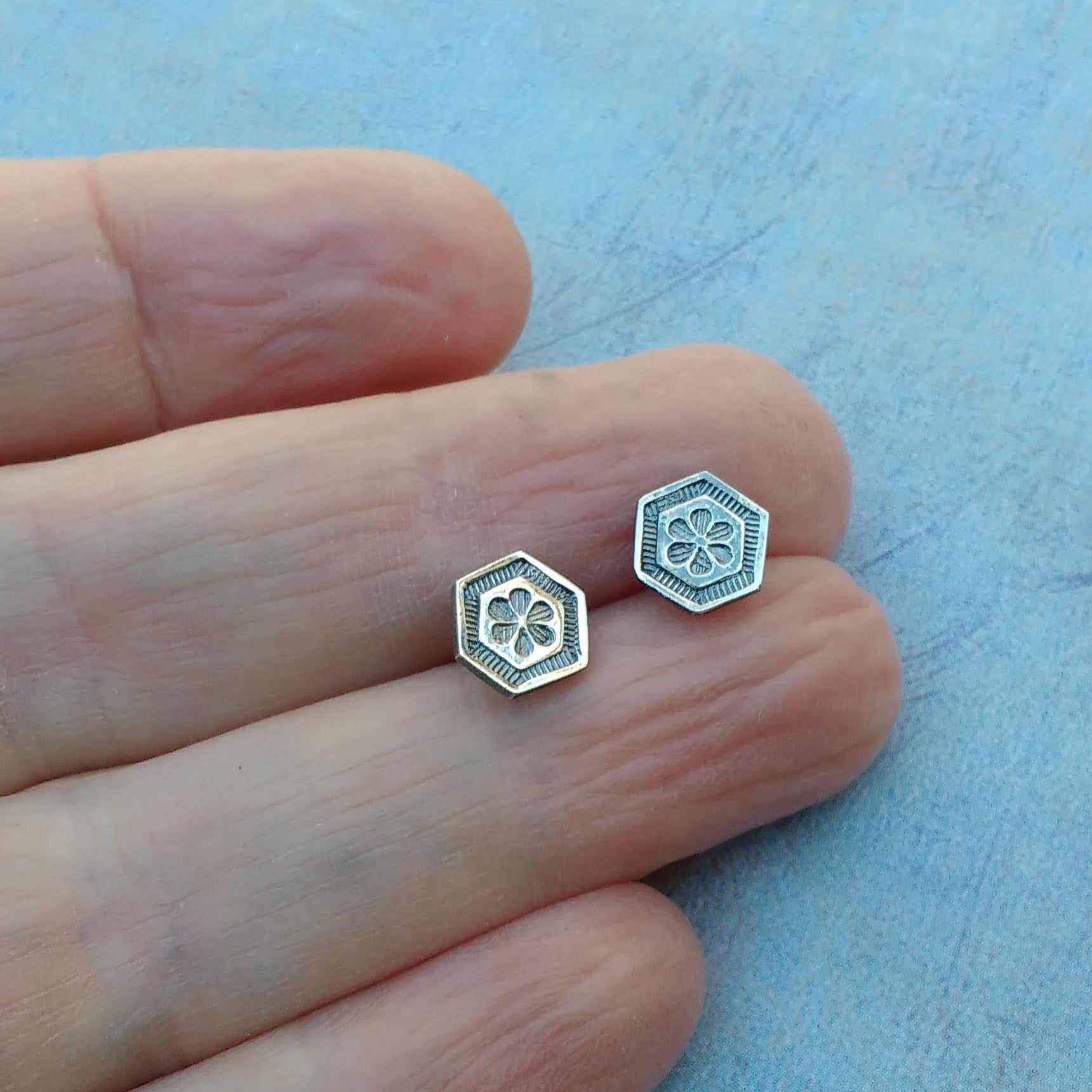 Floral hexagon stud earrings shown on hand for scale