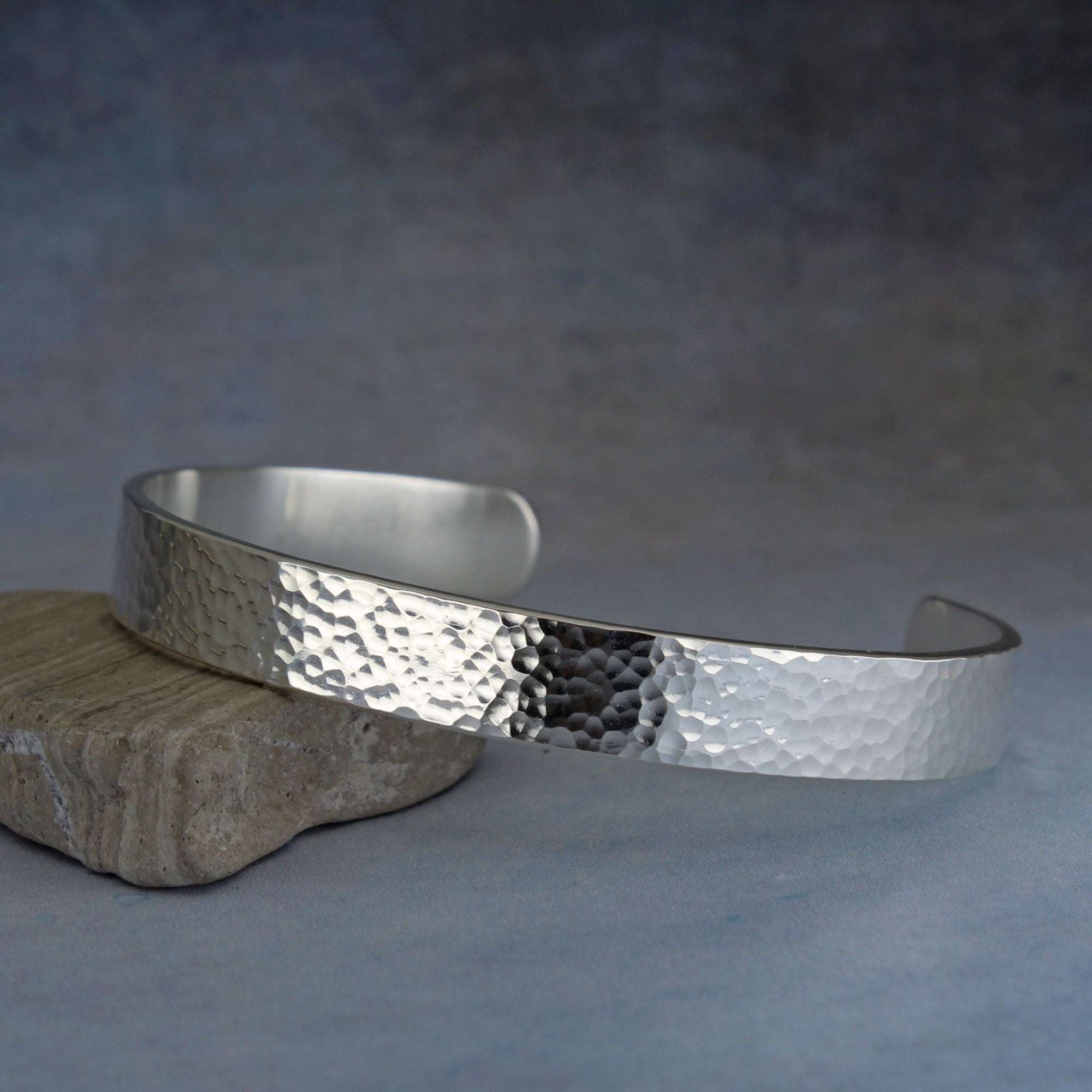 Silver hammered bracelet on a textured surface with personalized inscription