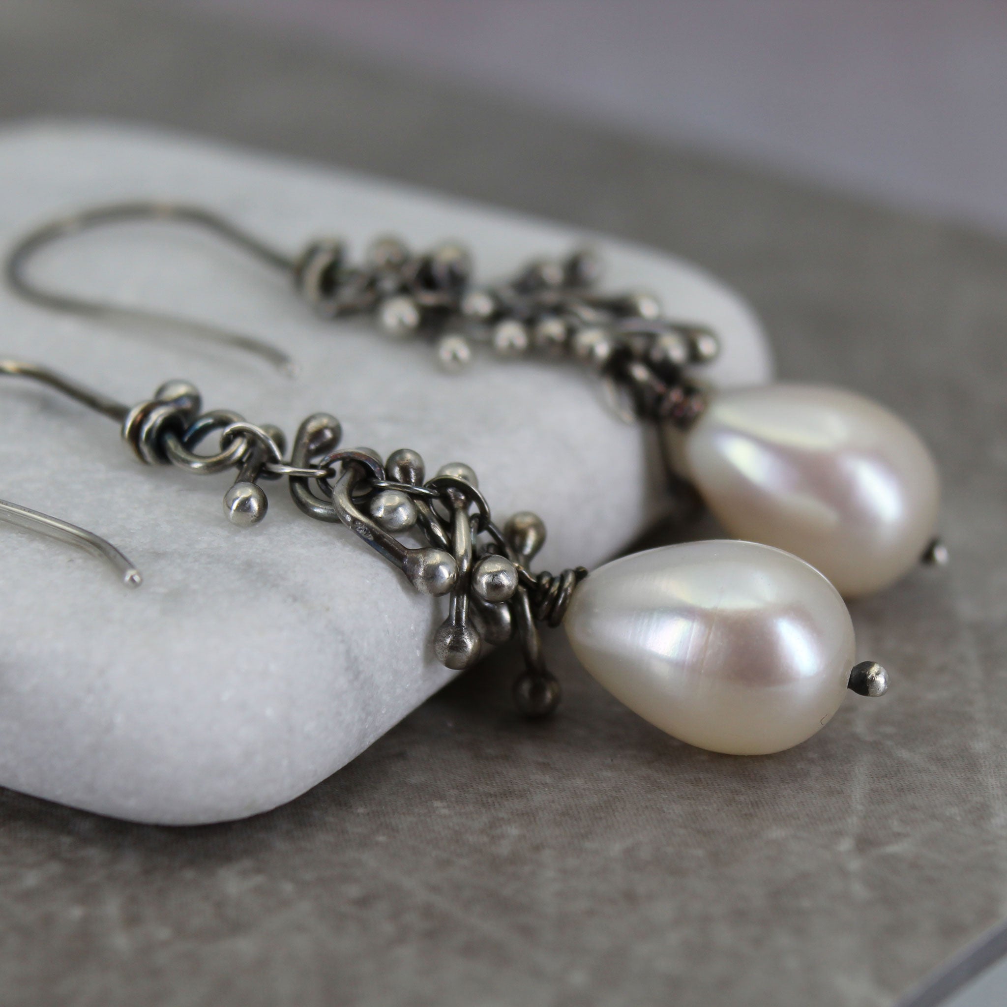 Pearl earrings with silver chain details on a stone surface