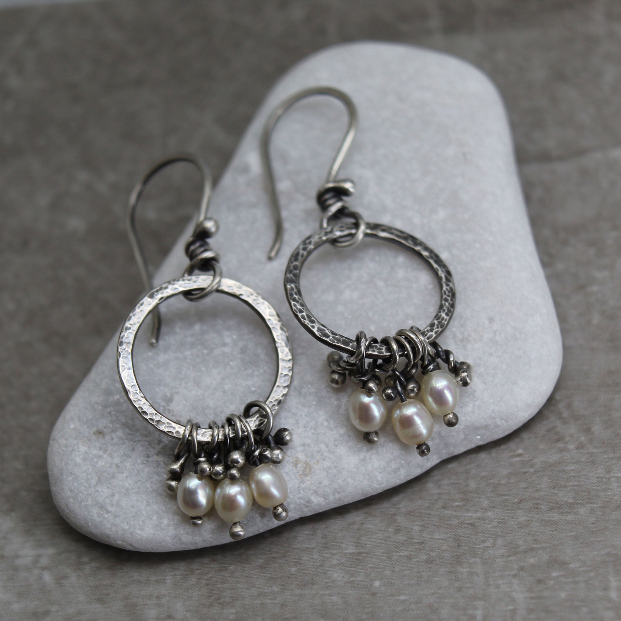 Silver hoop earrings with pearl charms on a stone surface