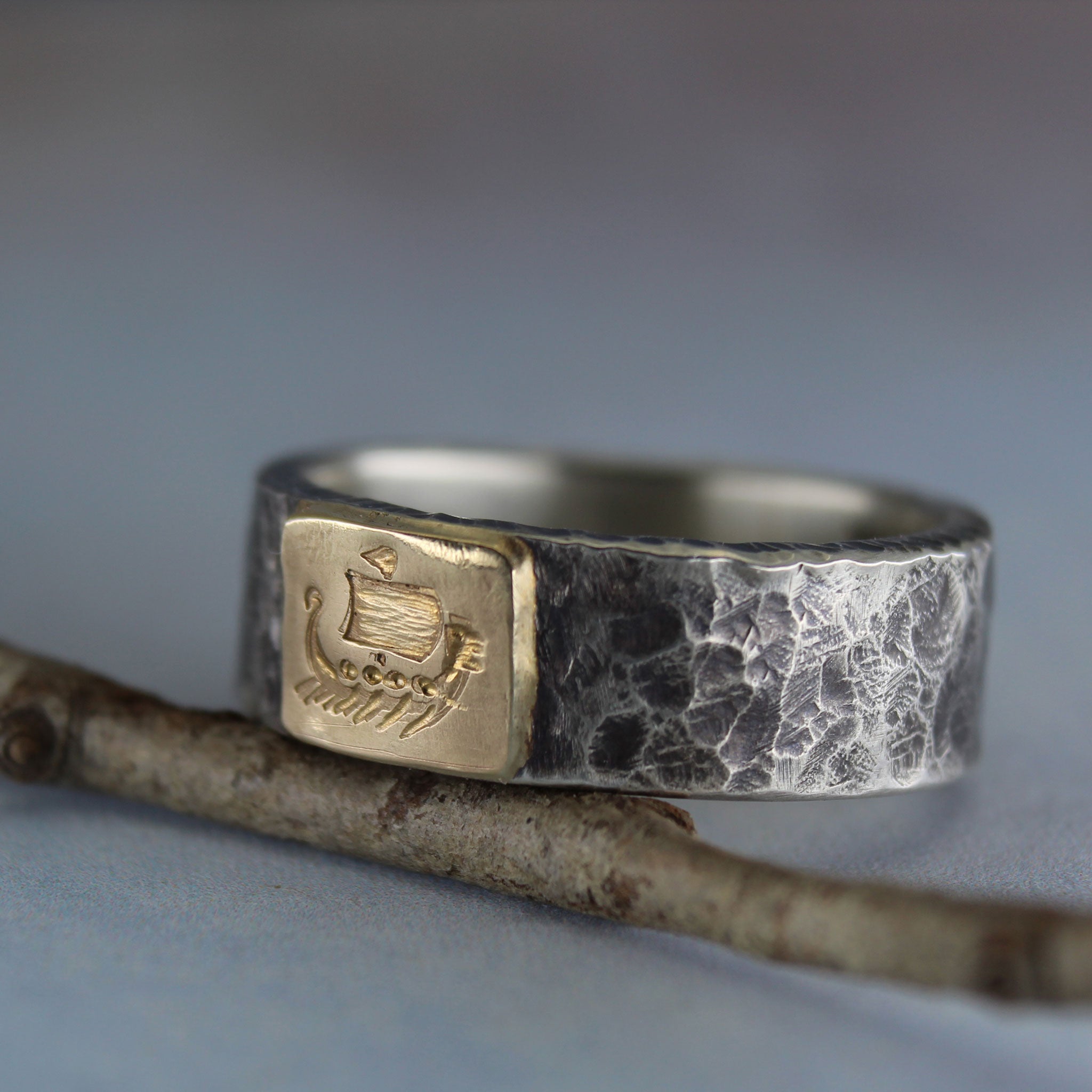 Viking ship symbol on gold tab, sterling silver ring resting on a twig