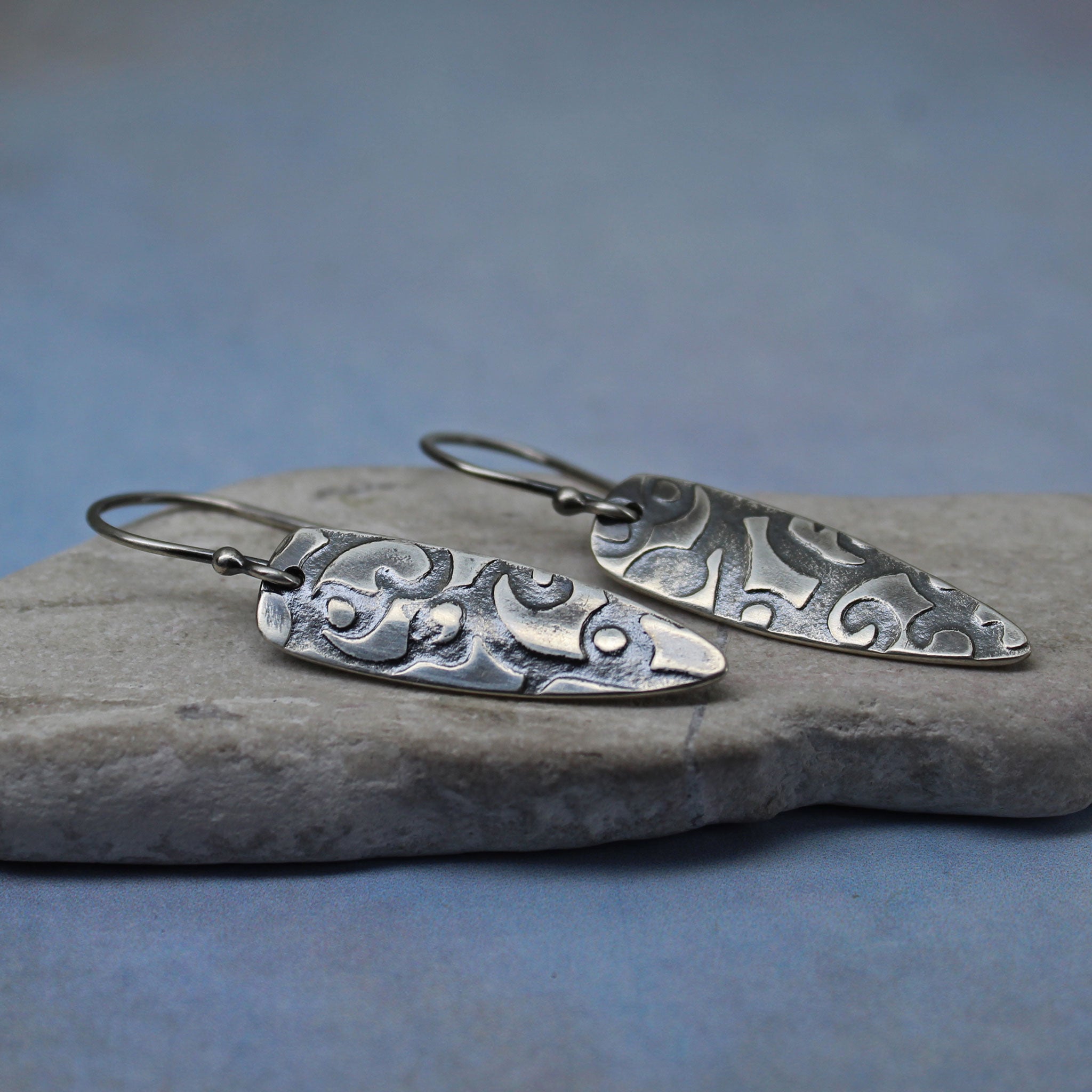 Side view of handcrafted sterling silver shield earrings with patina.