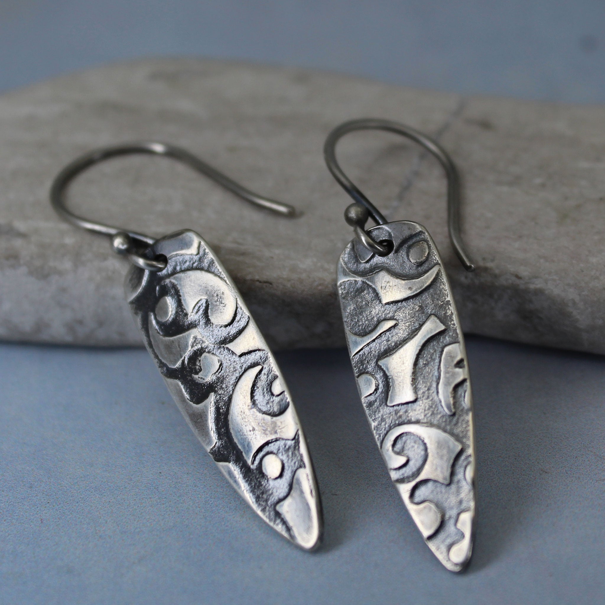 Close-up of abstract textured pattern on sterling silver shield earrings.