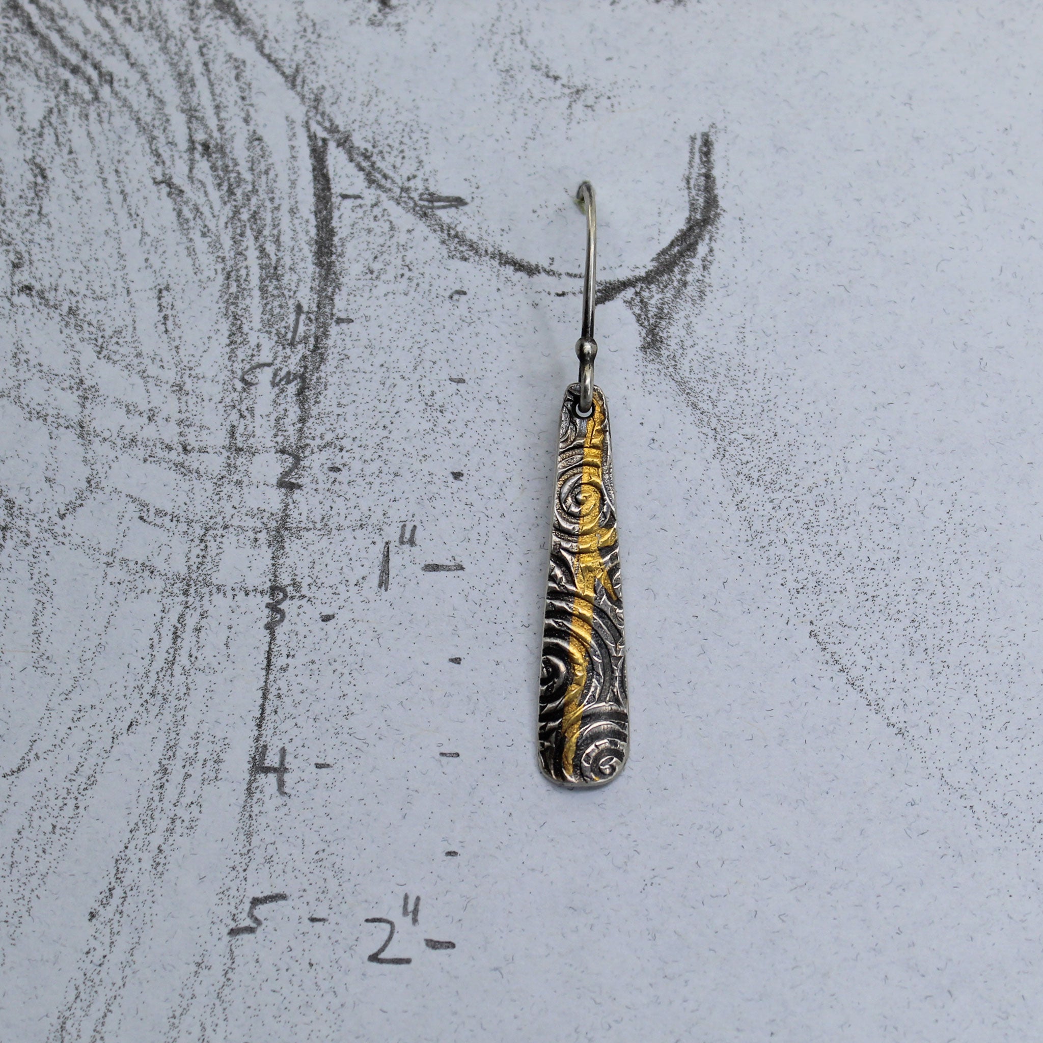 Handmade earrings with a embossed spiral pattern shown on a life size drawing of an ear.