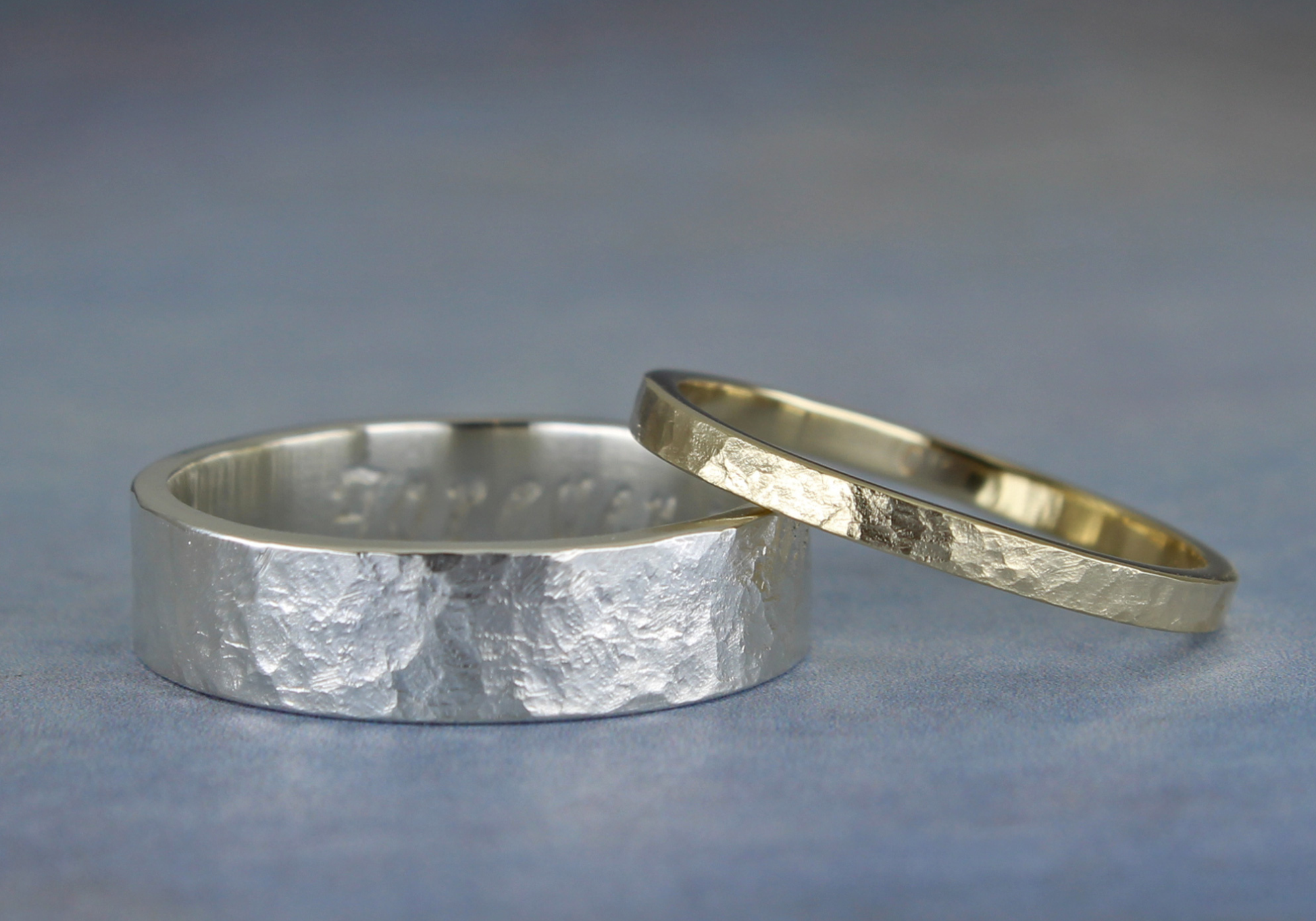 One gold and one silver ring with rustic hammered surfaces. An inscription is partially visible inside of the silver ring. 